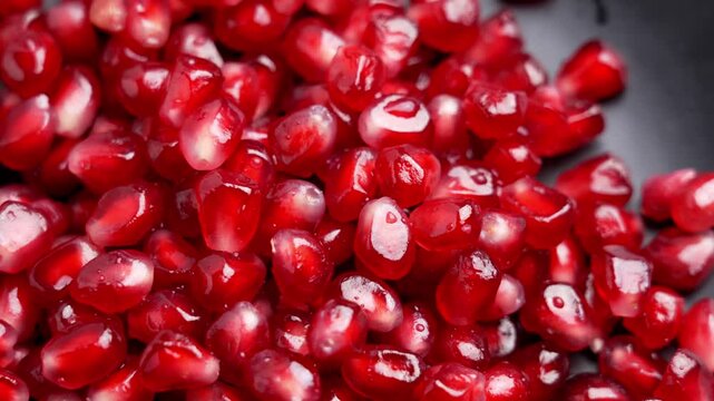 Pile of pomegranate seeds close up. Bright red arils on black ceramic plate. Rotation
