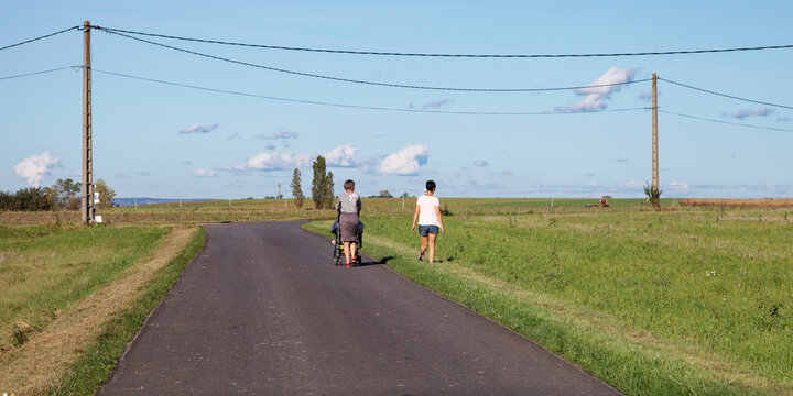 Grand-m&egrave;re, m&egrave;re et enfant dans une poussette promenant le long de la route en rase campagne