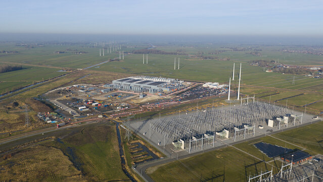 Groningen, Netherlands - 20 January 2026: Aerial view of Datacenter Westpoort and a large electrical substation surrounded by green fields and wind turbines under a clear sky.
