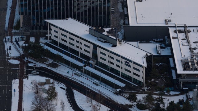 Veldhoven, Netherlands - 04 January 2026: Aerial view of ASML Building 7 with its modern architecture and logo, surrounded by snow-covered grounds and roads in winter.