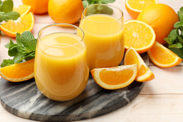 Citrus juice in glasses, fresh oranges and mint leaves on light wooden table, closeup © New Africa