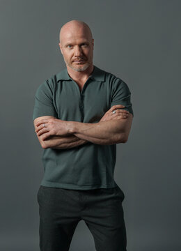 Confident mature bald man in dark green polo shirt looking aside on dark background, studio portrait with dramatic lighting