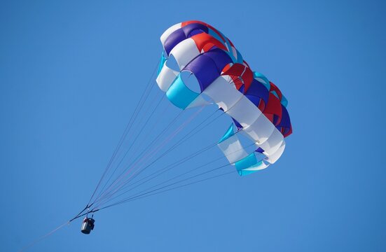 Colorful parasail with red, white, blue, and purple panels suspended in clear sky with lines converging at a central harness near Anna Maria Island, Florida, U.S.A