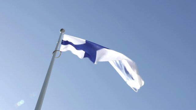 Finnish national flag waving on a flagpole against a clear blue sky. Low-angle view highlighting the Nordic cross symbol, representing Finland&rsquo;s identity, independence, and cultural heritage.