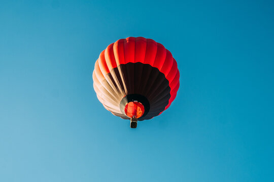 View of a vibrant red and black hot air balloon contrasts against the serene, cloudless azure sky, capturing a moment of peaceful flight, Kikinda, Vojvodina, Serbia.