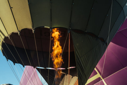 View of a vibrant orange flame bursting forth to inflate a multicolored hot air balloon against a clear blue sky, Kikinda, Vojvodina, Serbia.