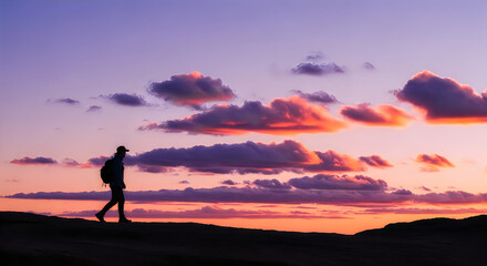 Fototapeta premium A lone person’s silhouette against a vibrant sunset sky, walking on a distant horizon, evokes peace and the grandeur of nature's evening display