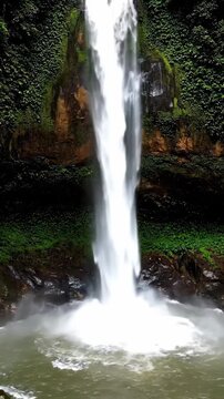 Majestic Tropical Waterfall with Powerful Water Stream Falling from a Lush Green Cliff into a Misty Pool for Travel Vlogs and Nature Documentaries. Vertical. Video. Portrait Orientation.