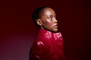 Profile portrait of African American woman with dark skin wearing red leather jacket on dark red background. Concept of fashion, beauty, confidence, and elegance in studio lighting. © SHOTPRIME STUDIO