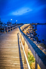 Naklejka premium Illuminated wooden walkway by the sea after sunset at blue hour