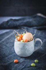 Stoneware cup with colored egg and colored chocolate eggs on a dark background © Daniela Baumann