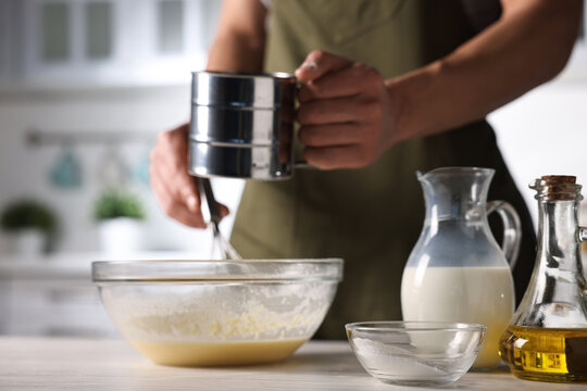 Making dough. Man sifting flour into bowl at light wooden table, closeup