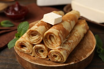 Tasty rolled crepes with butter and mint leaves served on wooden table, closeup © New Africa