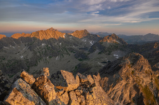 View of jagged peaks kissed by the golden sunrise, casting long shadows across the rugged landscape, a symphony of light and stone in Vysoke Tatry, Presovsky kraj, Slovakia.