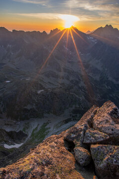 View of jagged peaks silhouetted against a vibrant sunrise, as golden light bursts across the sky illuminating the rugged terrain, Vysoke Tatry, Presovsky kraj, Slovakia.