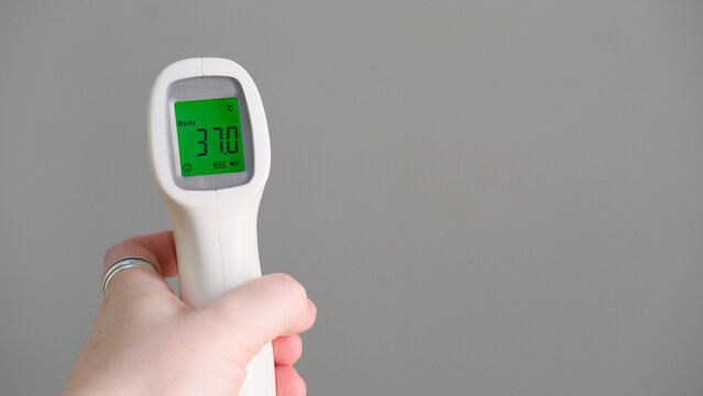 Hand holding infrared thermometer for temperature measure showing subfebrile 37 celsius degrees on green screen. Remote measurement of fever for children and public places, copy space. Flu season