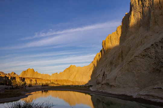 View of golden sunlight kissing the rugged cliffs reflected in the tranquil waters, contrasting against the clear blue sky, Hingol National Park, Balochistan, Pakistan.