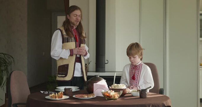 Man With Kid Boy Praying Before Dinner. Family in Ukrainian Traditional Attire Childhood. 4K 10-bit
