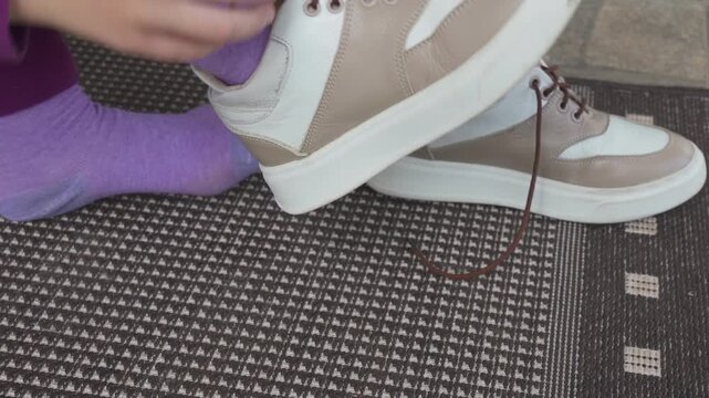 Little child learns to untie shoelaces on leather sneakers, close-up of hands, Child untying shoelaces on leather sneakers at the doorstep.Little girl in purple pants taking off her shoes after a walk