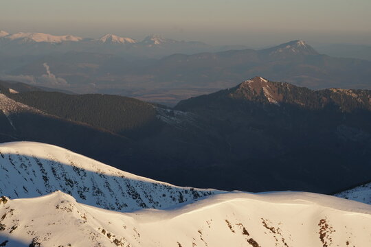 Aerial view of snow-capped peaks and dark valleys create a striking contrast in the mountainous landscape, Nizke Tatry, Zilina Region, Slovakia.