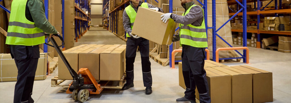 Warehouse workers move boxes for inventory stocktaking. Team uses a pallet jack between racks, managing storage and orders for shipping and delivery. Logistics teamwork inventory control theme.