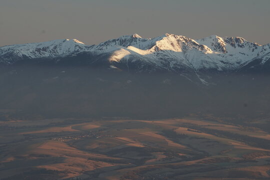 Aerial view of snow-capped peaks kissed by the sun, casting long shadows on the rugged landscape, creating a serene yet formidable vista, Nizke Tatry, Zilina Region, Slovakia.