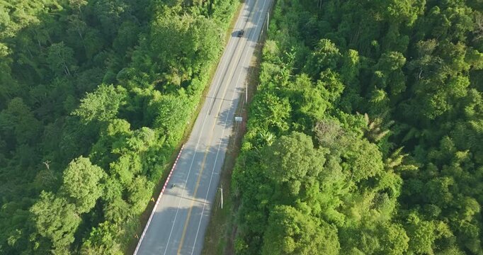 An aerial view of a scenic winding road cutting through lush green mountains and rolling hills under a clear blue sky. The landscape conveys adventure, travel, and the natural beauty of rural