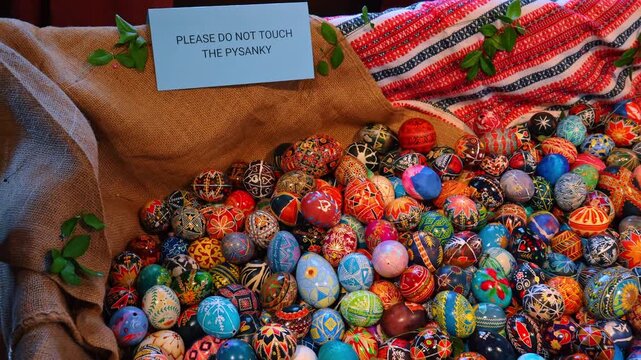 Collection of traditional Ukrainian Pysanky Easter eggs on burlap. Large pile of hand-painted Pysanky eggs with intricate patterns on brown burlap next to a warning sign in New York.