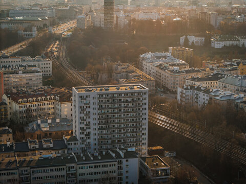 Aerial view of buildings and railway tracks bathed in the warm glow of the setting sun, creating a striking contrast between light and shadow, Warsaw, Poland.