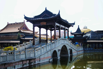Fototapeta premium Elegant curved stone bridge with traditional Chinese pavilion in a cultural complex, surrounded by classic architecture.