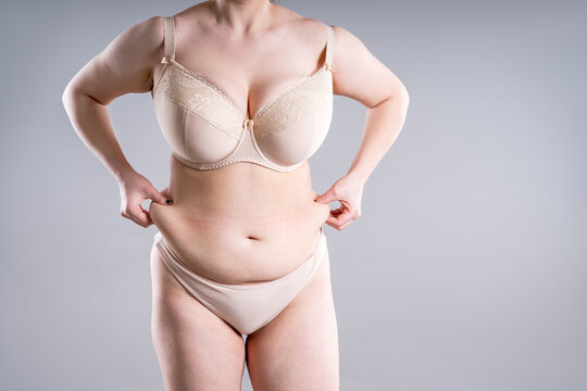 Unrecognizable plus size woman in beige lingerie pinching belly fat. Concept of weight loss, diet and liposuction