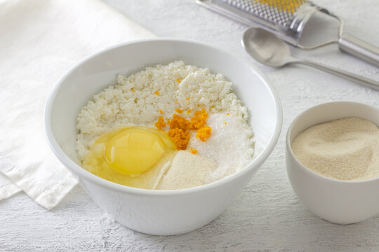 Ingredients for ricotta cheese filling in white bowl with raw egg orange zest semolina and sugar on kitchen table