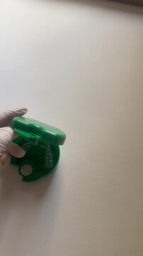 Close-up vertical video of a gloved hand opening a green storage case and removing a transparent dental aligner on a white background