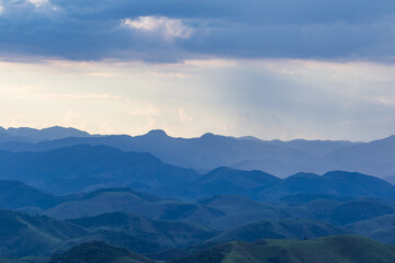 Obraz premium Layered Mountain Ranges Under Soft Rain and Dramatic Blue Sky