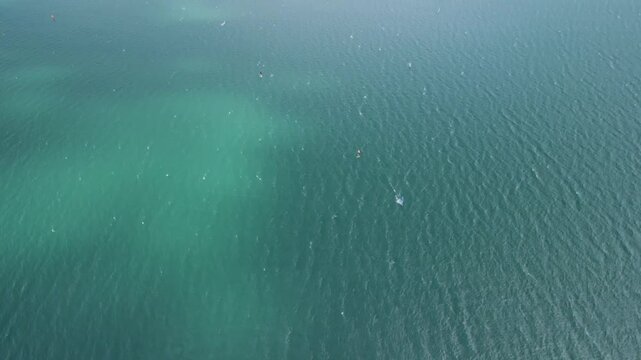 Drone aerial panorama of Lake Garda and Riva del Garda in northern Italy, camera rises above green cliffs to reveal turquoise lake water dotted with sailboats and the lakeside town