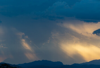 Fototapeta premium Sun Beams Breaking Through Storm Clouds Over Distant Mountains