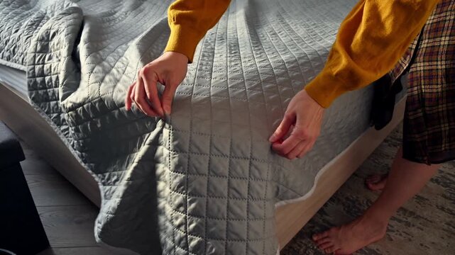 Woman arranging quilt on bed, showcasing bedding and bedroom decor details