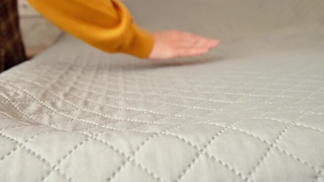 Hand smoothing quilted blanket on bed, showcasing fabric texture and detail