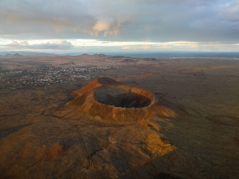 Aerial view of the stark volcanic crater under a soft, diffused sky casts long shadows over the arid landscape, Fuerteventura, Canarias, Spain.