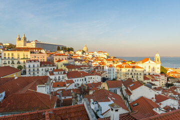 Fototapeta premium Alfama Oldest Historic Neighborhood at Sunset. Red Roofs and White Houses. Vibrant Lisbon Old Town, Portugal. View from Miradouro das Portas do Sol. Wide Shot