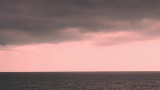 Time lapse of dramatic pink sunset sky with rain storm black thunderclouds over the sea motion. Ocean, tropical sunset sky dark clouds 4K timelapse horizon, bad weather on the beach, humid tropical cl