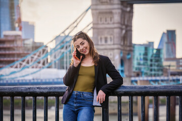 Fototapeta premium A young, city life woman talks at her mobile phone in front of the skyline of London