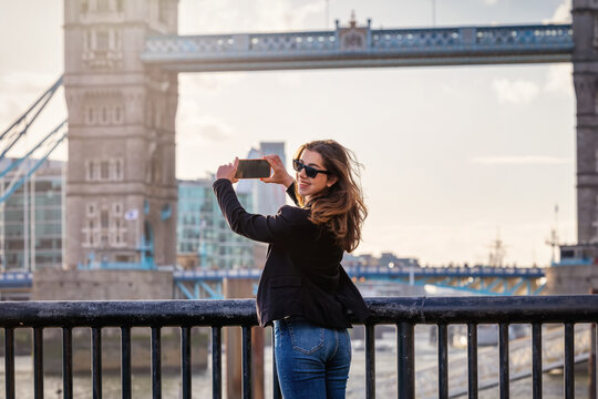 A happy tourist woman taking photos of the famous Tower Bridge in London, England, during her city vacations