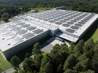 Fototapeta premium Solar panels cover the roof of a large building in a forested area, supporting renewable energy production for a cleaner future.