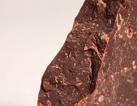 Raw cocoa mass block photographed close up showing natural texture and structure. Dark cocoa ingredient used for chocolate production.