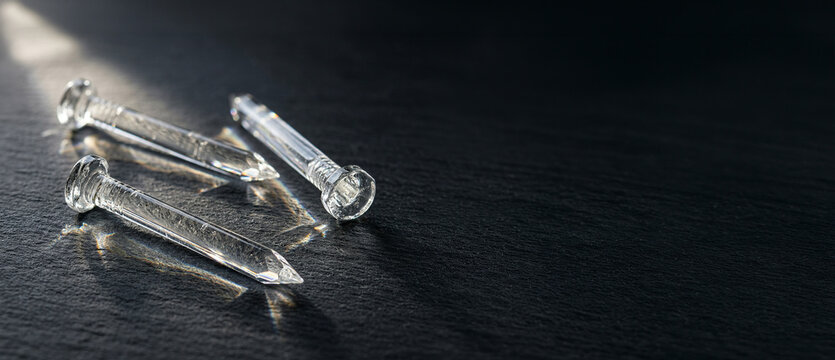 Transparent glass nails lying on dark surface with light reflections, close up abstract objects, industrial concept, minimal design, sharp detail