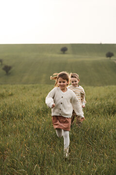 Two children, a boy and girl, playing tag in green fields, running, laughing, and chasing each other, enjoying outdoor fun and sunny summer freedom.