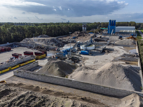 Aerial view of an industrial site with piles of sand and gravel contrasting against the green trees, Almere, Flevoland, Netherlands.