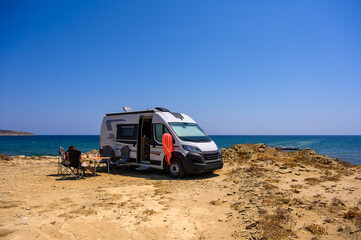 A family of travelers relaxes in folding chairs next to their modern campervan on a rugged beach in...
