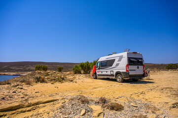 Obraz premium A family of travelers relaxes in folding chairs next to their modern campervan on a rugged beach in Limnos, Greece, enjoying a sunset view of the Aegean Sea during an off-grid motorhome road trip.